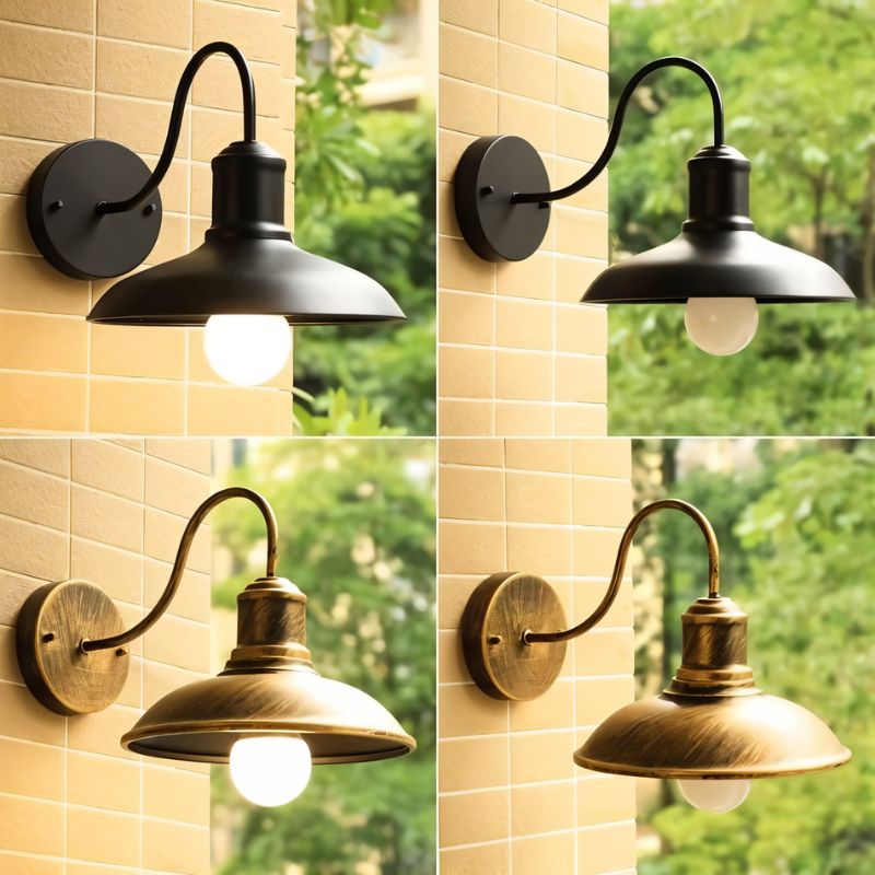 Four Clérachic gooseneck wall lamps, two in black and two in bronze, on a brick wall with foliage behind