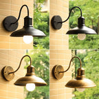 Four Clérachic gooseneck wall lamps, two in black and two in bronze, on a brick wall with foliage behind