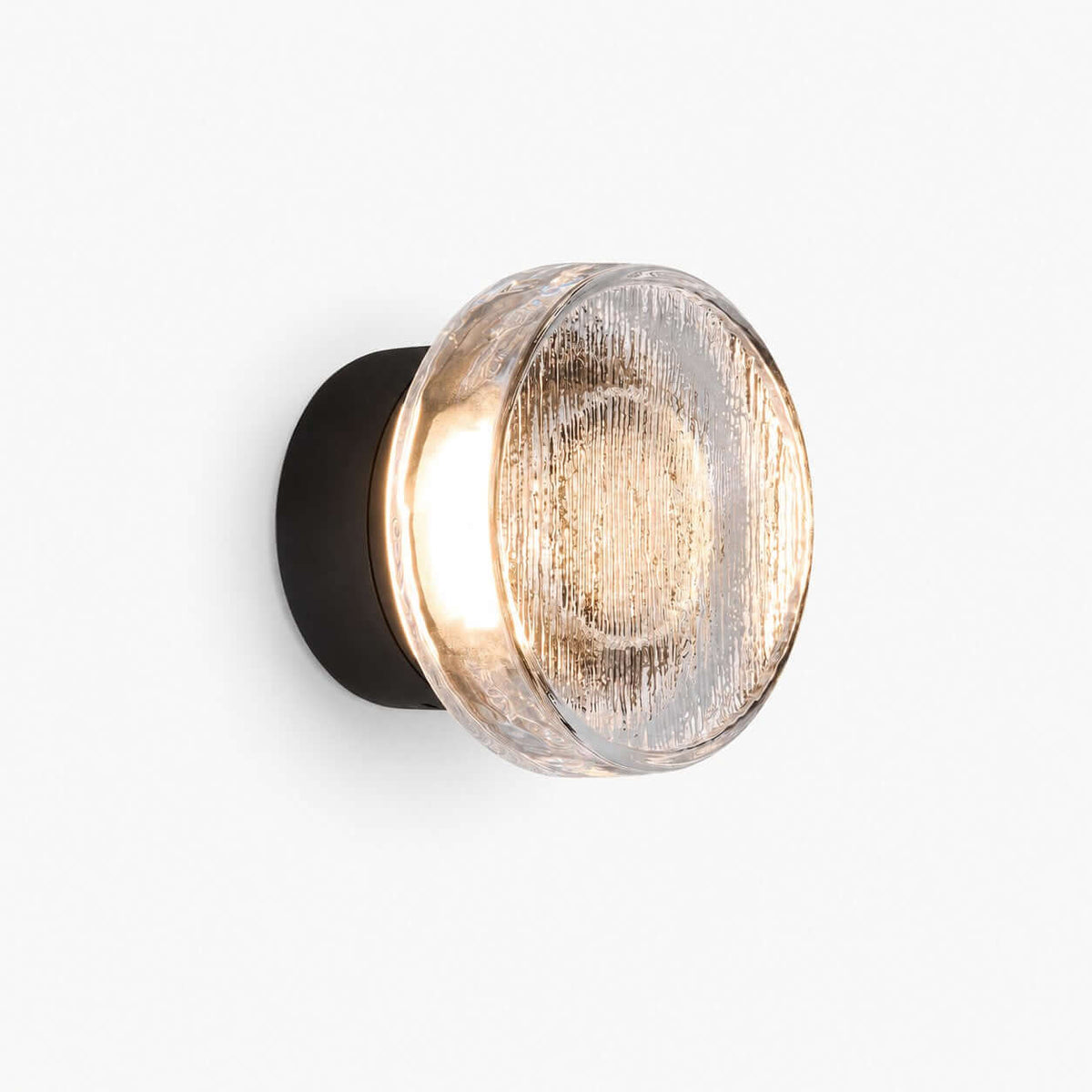 Round outdoor wall light with a clear ribbed glass diffuser on a black backplate, lit warm, on a plain white backdrop, from Clérachic.