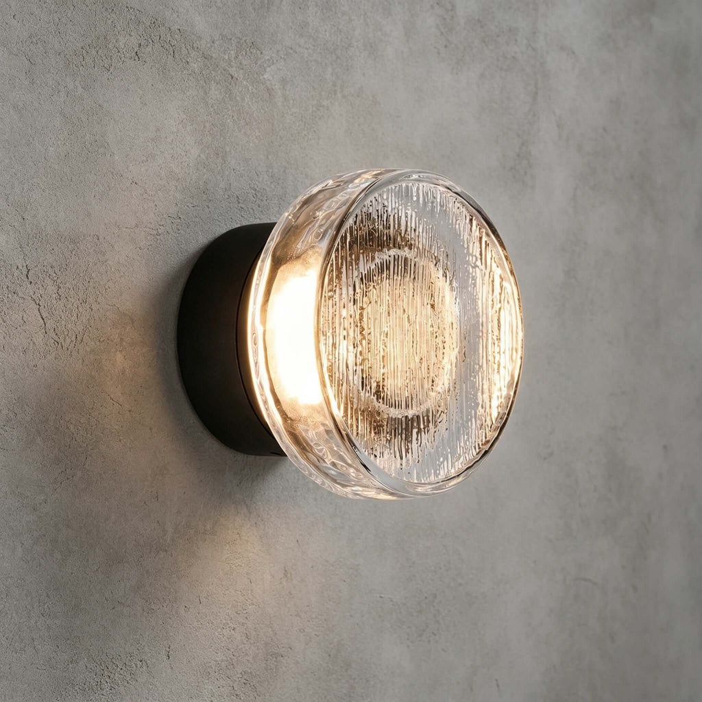 Close view of the clear ribbed glass diffuser on this Clérachic outdoor wall light, lit warm on a grey plaster wall.