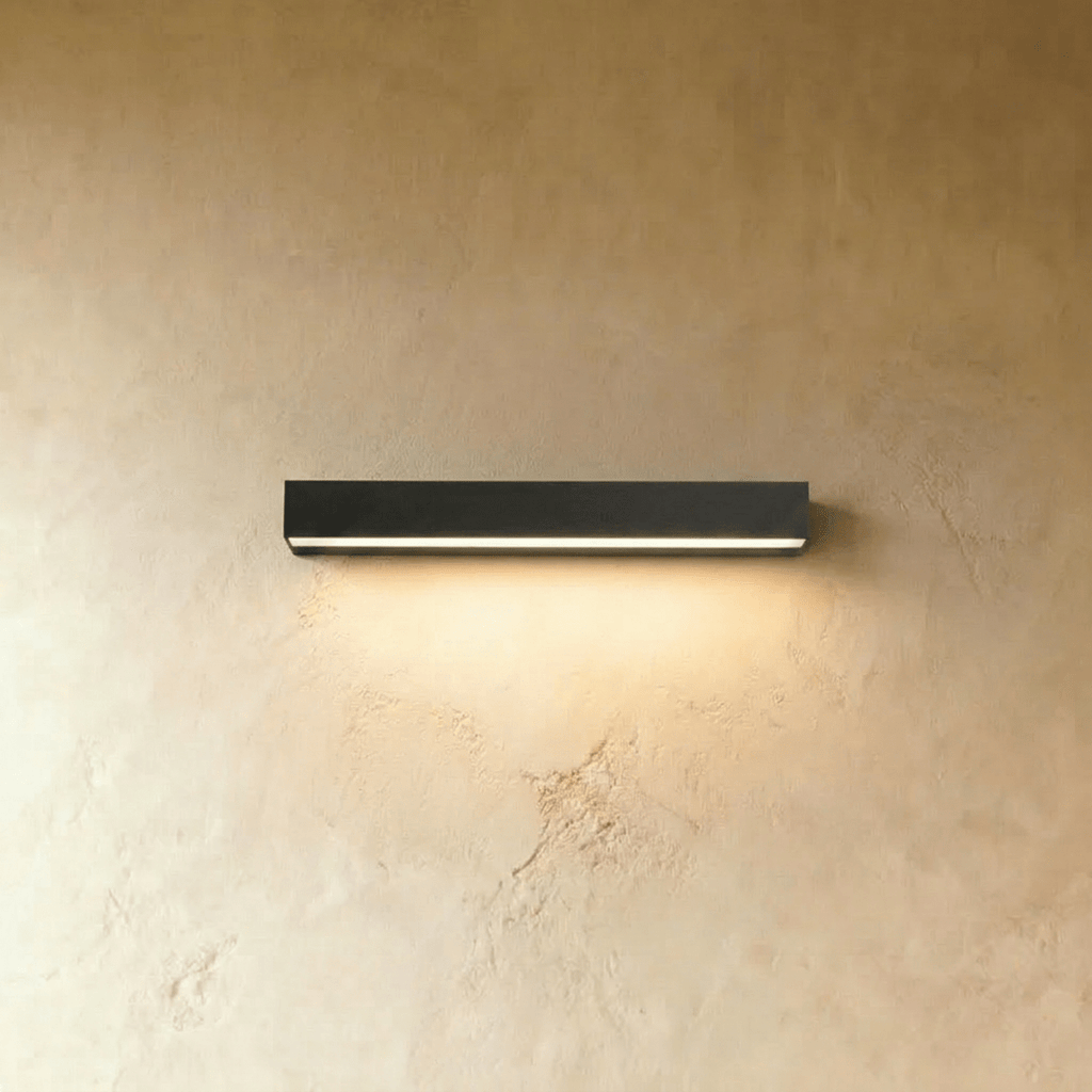 Clérachic slim black rectangular wall light casting a soft warm wash of light down a limewashed wall.