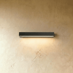 Clérachic slim black rectangular wall light casting a soft warm wash of light down a limewashed wall.