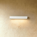 Clérachic slim white rectangular wall light casting a soft warm wash of light down a limewashed wall.