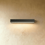 Clérachic longer slim black wall light with a lit diffuser strip glowing warm on a limewashed wall.