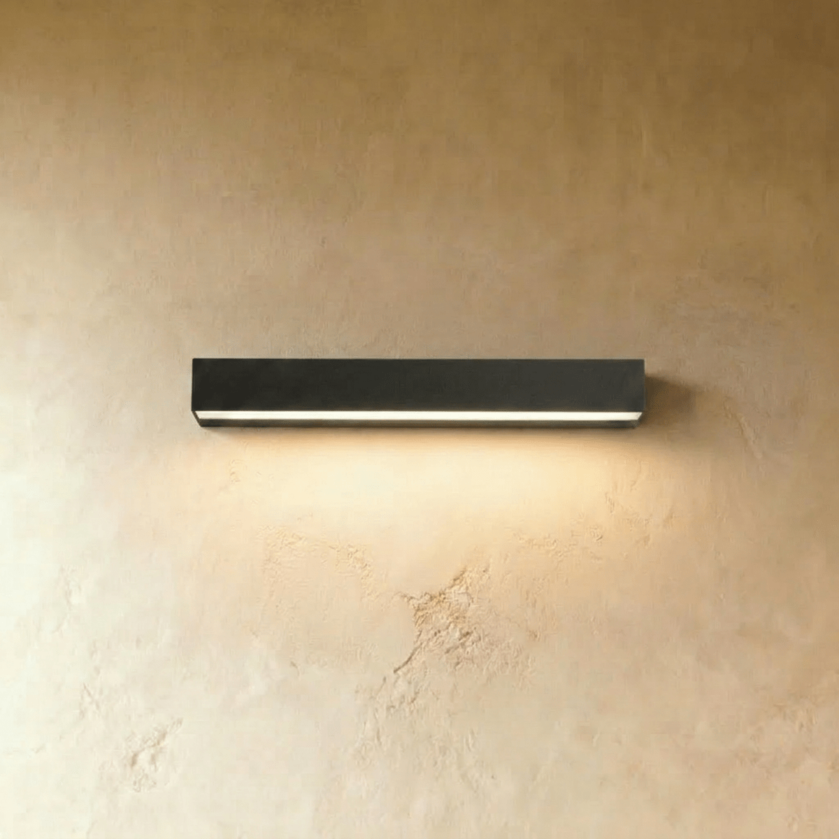 Clérachic longer slim black wall light with a lit diffuser strip glowing warm on a limewashed wall.