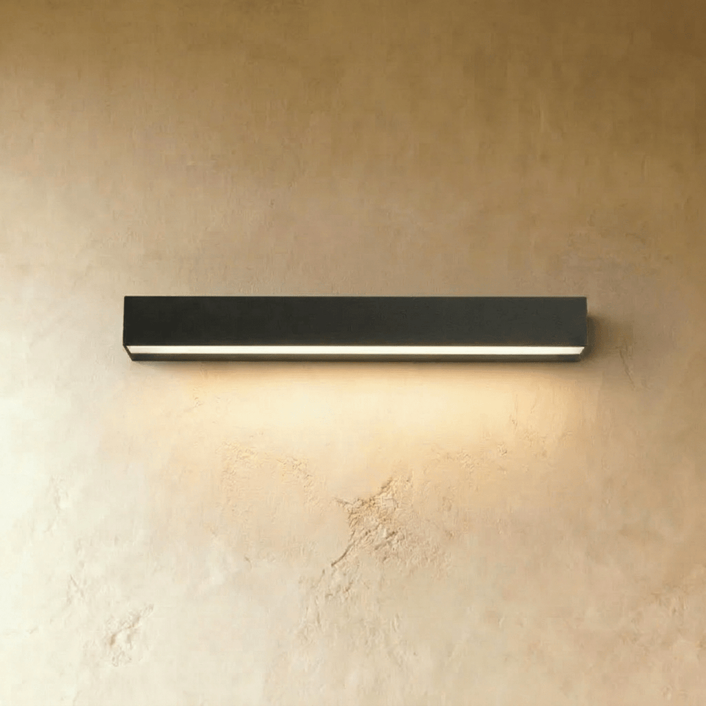 Clérachic longest slim black wall light in this set, its diffuser strip glowing warm above a limewashed wall surface.