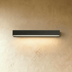Clérachic longest slim black wall light in this set, its diffuser strip glowing warm above a limewashed wall surface.