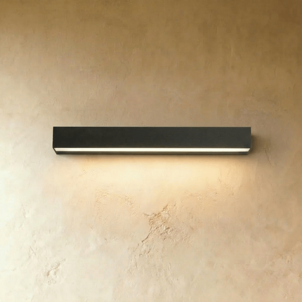 Clérachic longest slim black wall light in this set, its diffuser strip glowing warm above a limewashed wall surface.