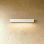 Clérachic longer slim white wall light with a lit diffuser strip, washing warm light down a limewashed wall.
