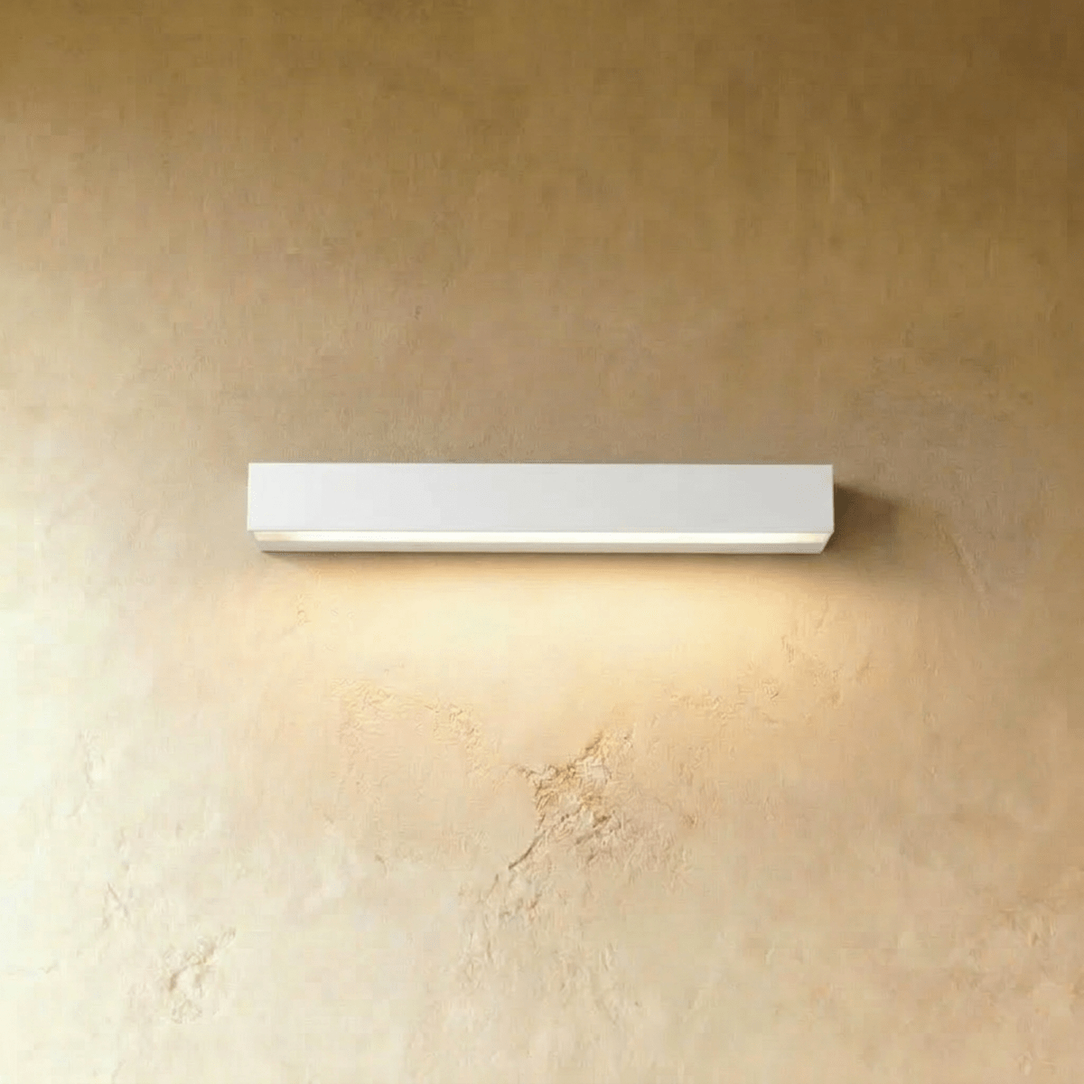 Clérachic longer slim white wall light with a lit diffuser strip, washing warm light down a limewashed wall.