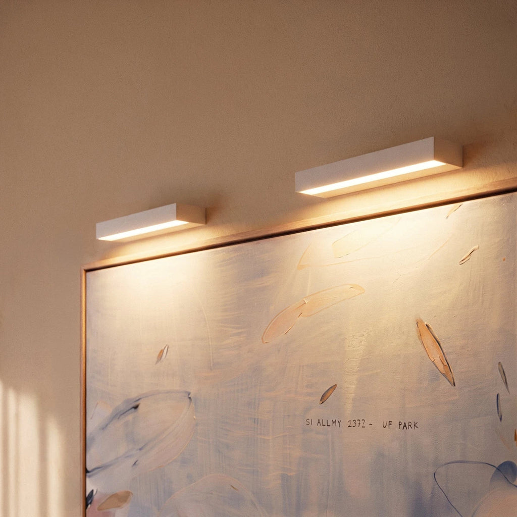 Close view of two Clérachic slim white wall lights glowing warm over the top edge of a framed painting.