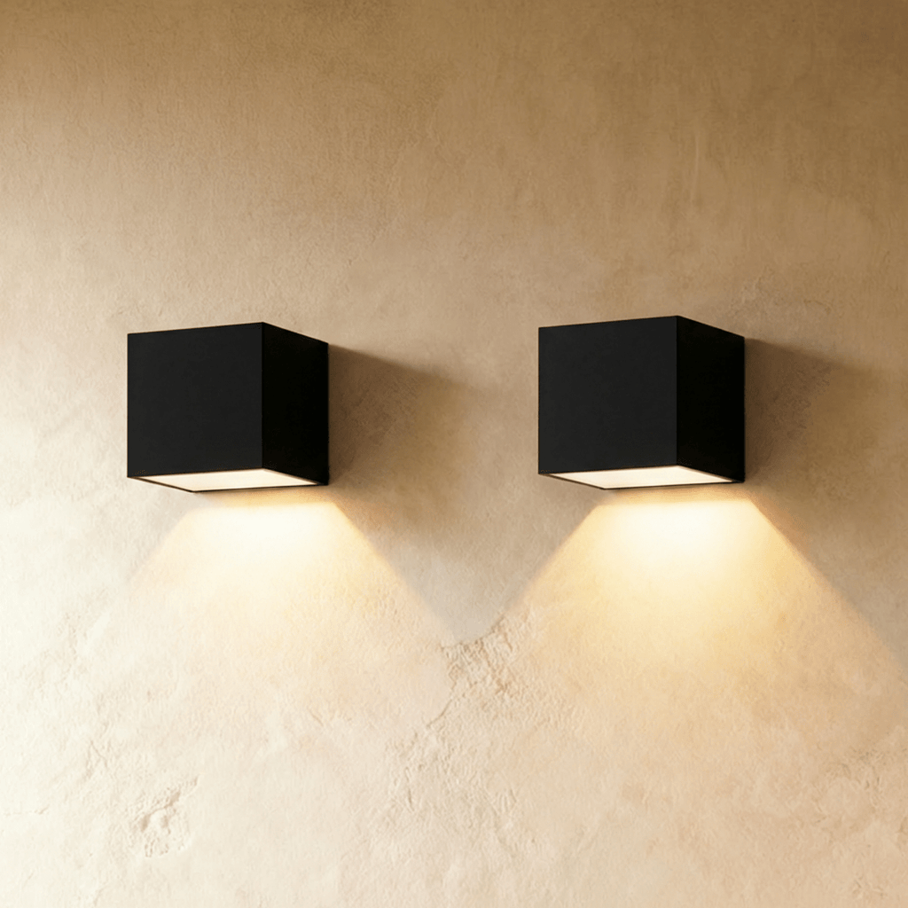 Pair of Clérachic black cube wall lights side by side on limewash plaster, each throwing a warm cone of light downward.