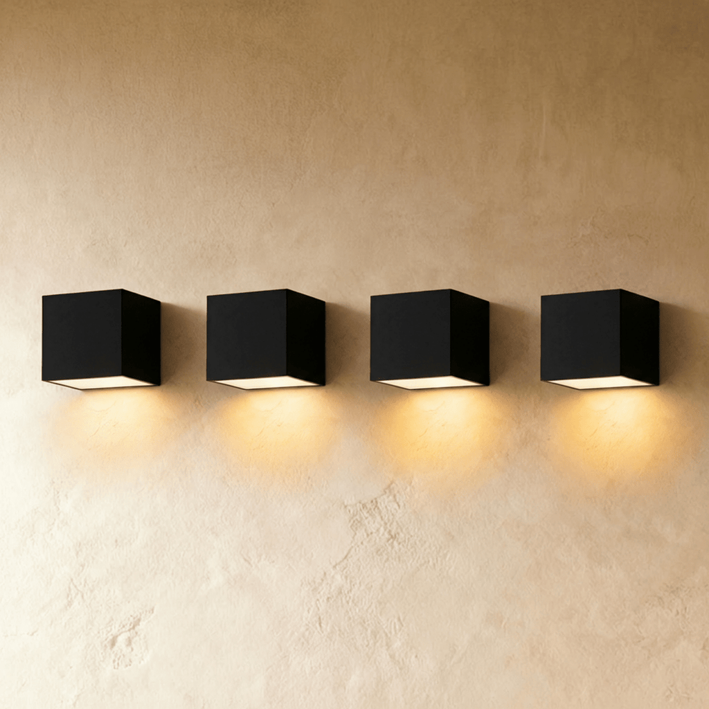 Row of four Clérachic black cube wall lights on a limewash plaster wall, each casting a warm pool of light below.