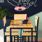 Clérachic oval blown glass pendant light in dusty pink glass lighting a pine café table under a chalkboard wall.