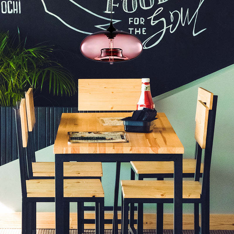 Clérachic oval blown glass pendant light in dusty pink glass lighting a pine café table under a chalkboard wall.