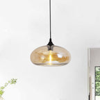 Amber glass Clérachic oval pendant light lit in a bright white room, warm bulb glowing through the shade beside a window.