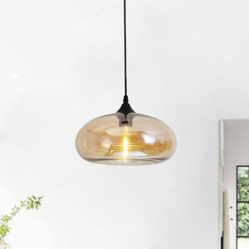 Amber glass Clérachic oval pendant light lit in a bright white room, warm bulb glowing through the shade beside a window.