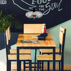 Clérachic oval blown glass pendant light in smoke gray above a wooden café table, its filament bulb mirrored in the glass.