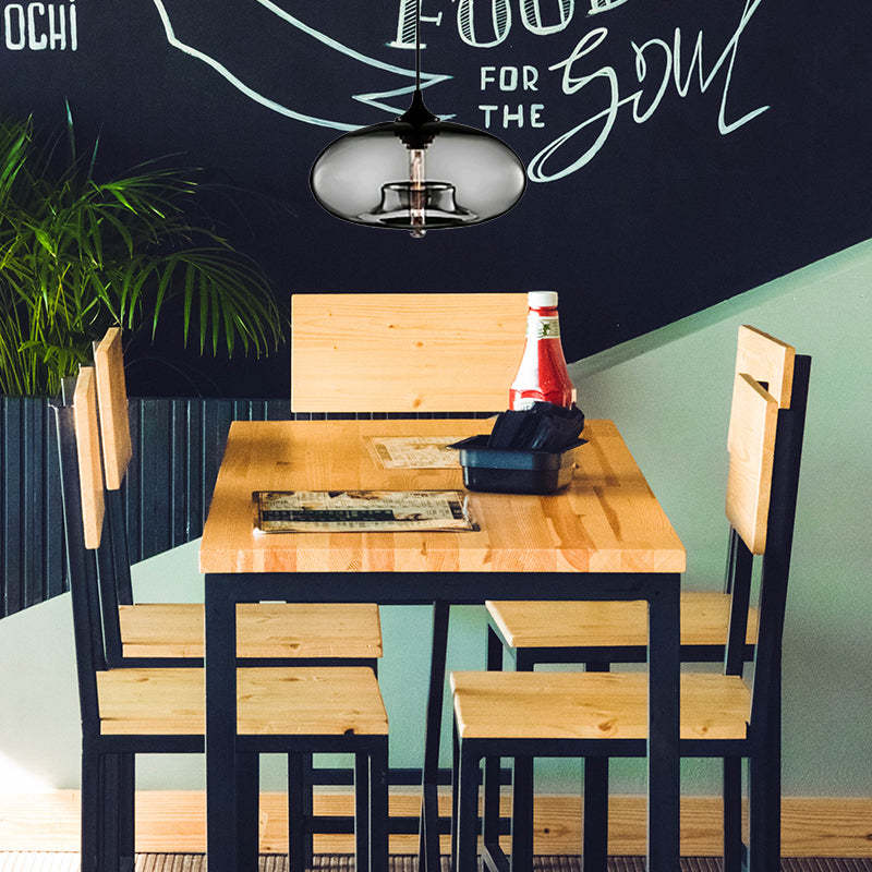Clérachic oval blown glass pendant light in smoke gray above a wooden café table, its filament bulb mirrored in the glass.
