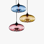 Three Clérachic oval blown glass pendant lights clustered at staggered drops in blue, amber and pink glass on white.