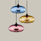 Blue, amber and pink Clérachic oval blown glass pendants hung at three heights against a warm taupe backdrop.