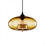 Deep amber Clérachic oval blown glass pendant light on white, the gold-toned shade catching light along its curve.
