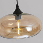 Close-up of the Clérachic oval pendant light showing the black cone socket cup and lit LED filament inside amber glass.