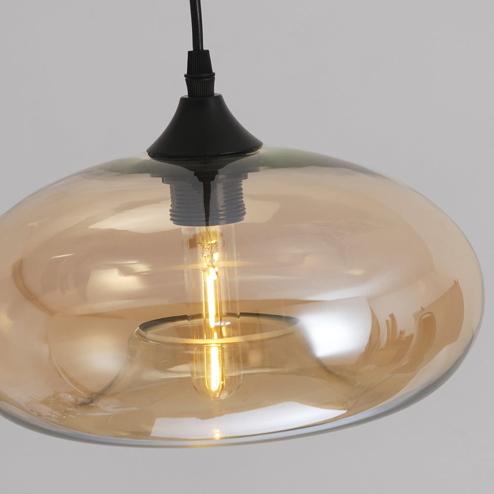 Close-up of the Clérachic oval pendant light showing the black cone socket cup and lit LED filament inside amber glass.