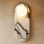 Clérachic wall light with an oval veined marble backplate and one lit frosted glass globe on a limewash wall.