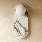 Clérachic wall light with an oval veined marble backplate and one unlit white glass globe on a plaster wall.