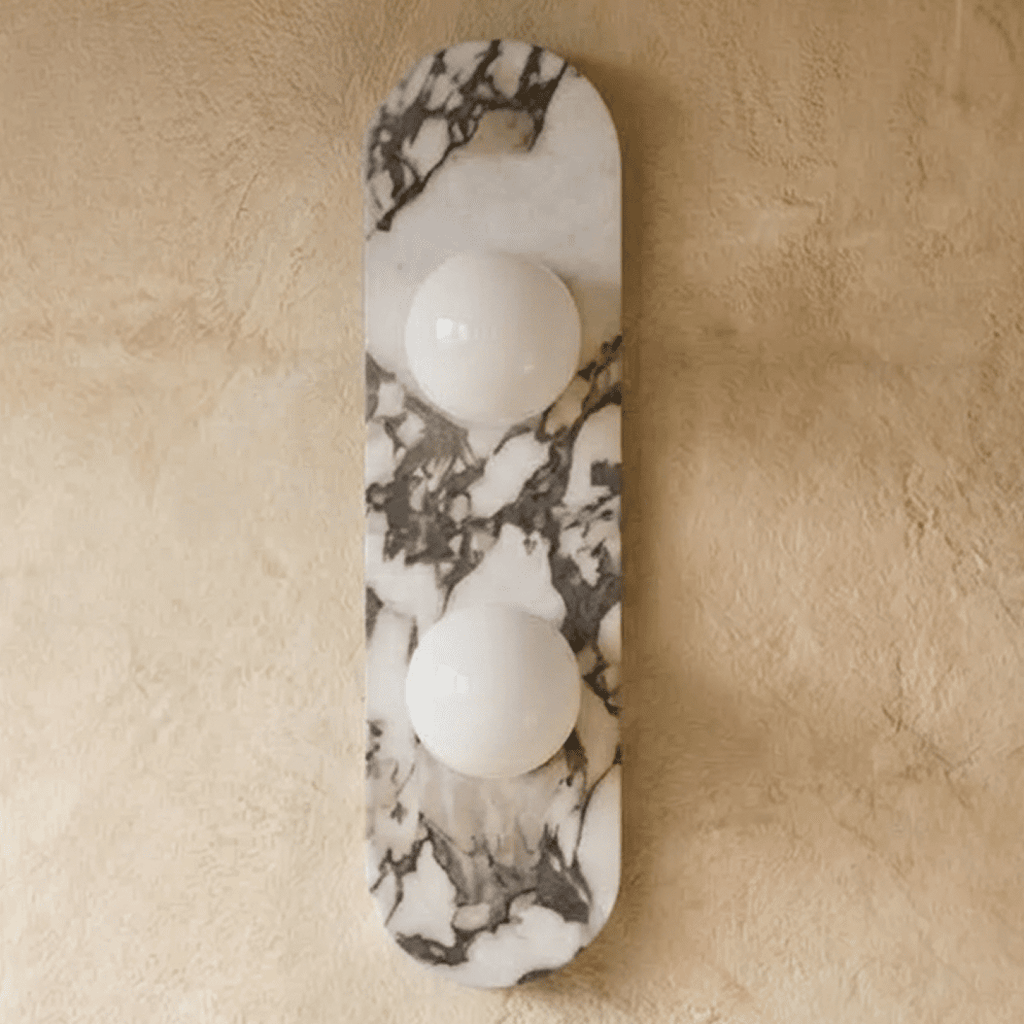 Clérachic two-globe wall light on a tall rounded marble backplate with grey veining, switched off on a plaster wall.