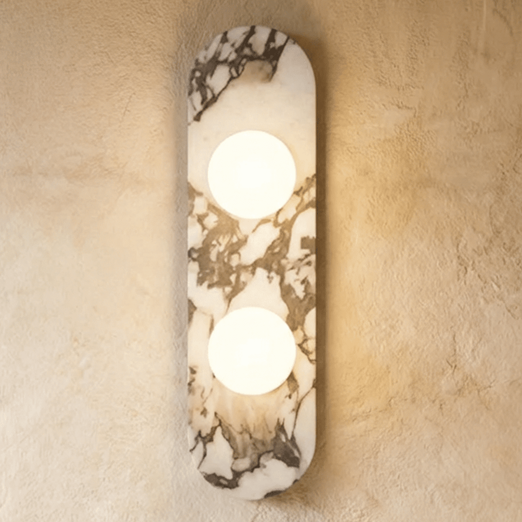 Clérachic two-globe wall light on a rounded marble backplate, both glass globes glowing warm on a plaster wall.