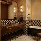 Clérachic pair of two-globe marble wall lights beside a large mirror, a marble-top basin unit and chequered tiles.