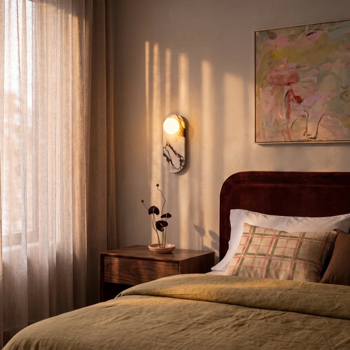 Clérachic one-globe marble wall light glowing above a walnut bedside table, with a velvet headboard and linen curtains.
