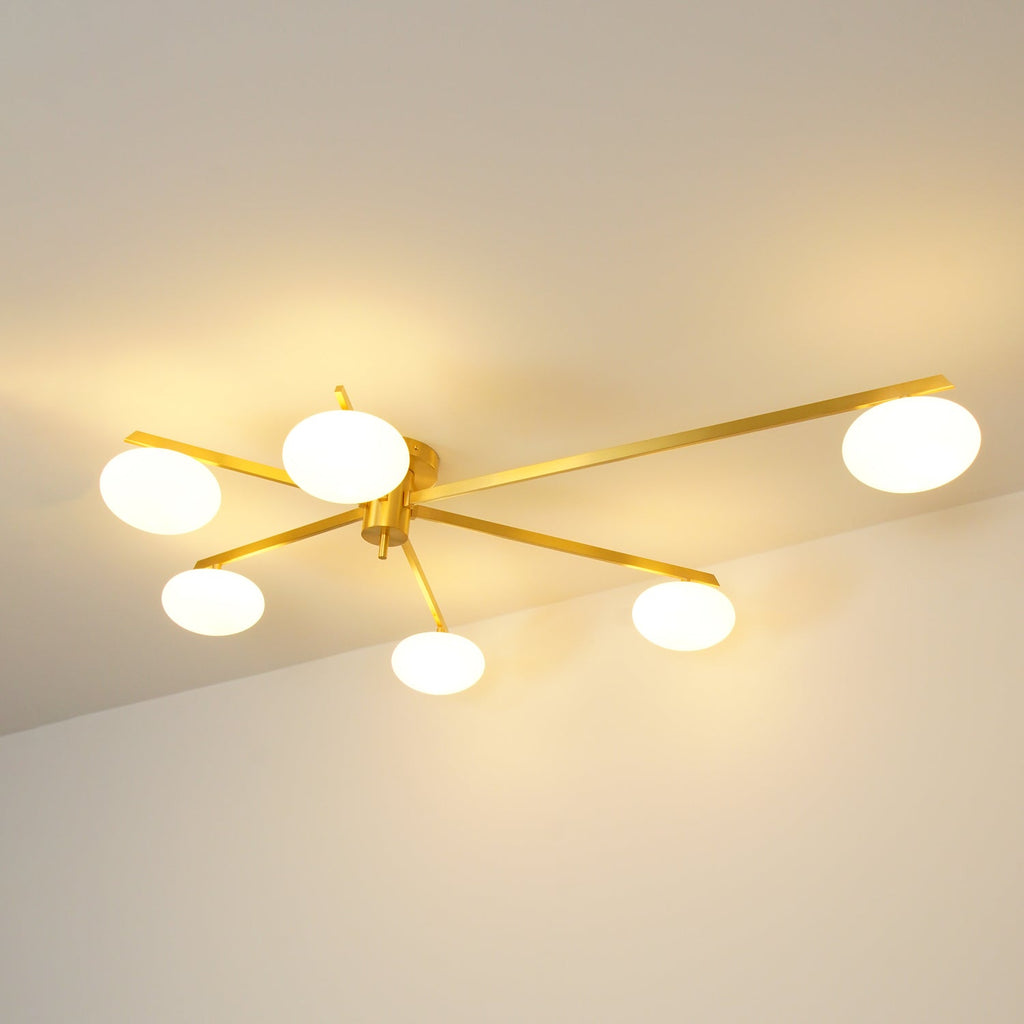 Clérachic Oval Opal Glass Ceiling Light in brass, six lit shades washing warm light across the ceiling of a dim room.
