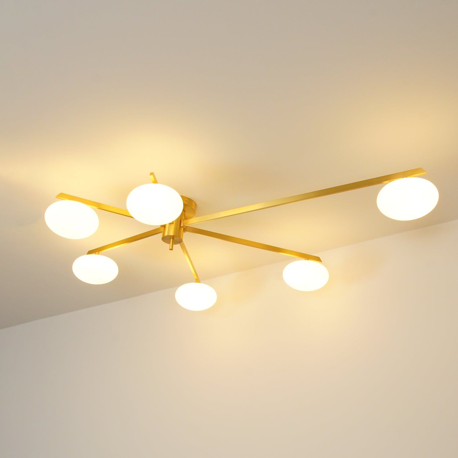 Clérachic Oval Opal Glass Ceiling Light in brass, six lit shades washing warm light across the ceiling of a dim room.