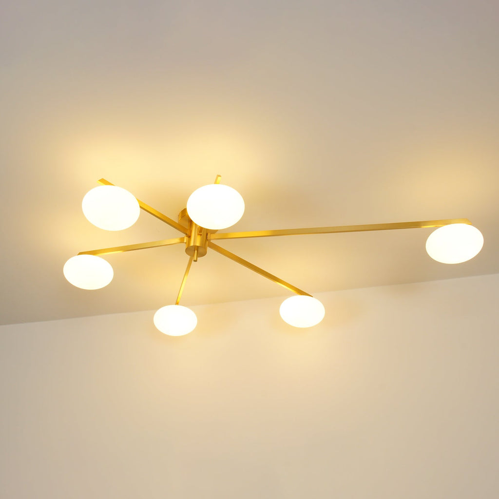 Clérachic Oval Opal Glass Ceiling Light lit in brass, six creamy ovals spreading a broad warm glow over a bare wall.