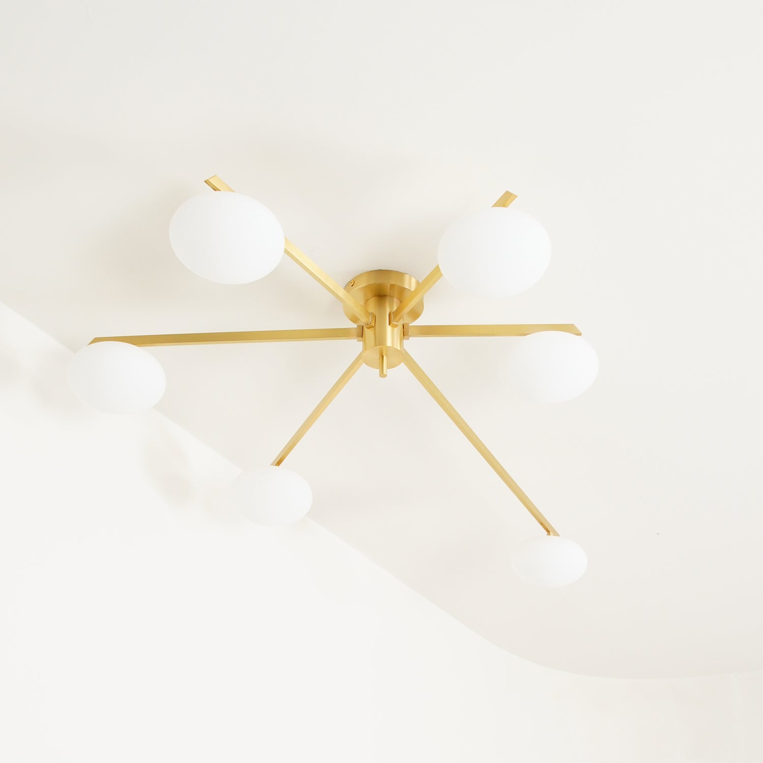 Clérachic Oval Opal Glass Ceiling Light in brass on a cream ceiling, its blade arms throwing a soft angled shadow.
