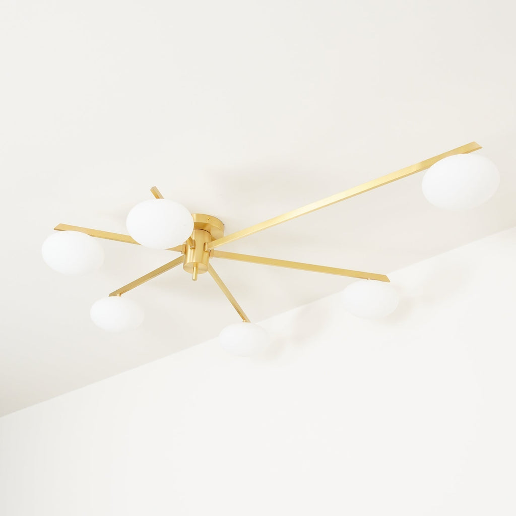 Clérachic Oval Opal Glass Ceiling Light in brass viewed from below, six arms radiating over a white corner ceiling.