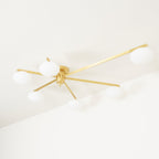 Clérachic Oval Opal Glass Ceiling Light in brass viewed from below, six arms radiating over a white corner ceiling.