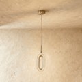 Clérachic single oval pendant with a brushed brass ring and textured clear acrylic shade, hanging on a fine cable against a plaster wall.
