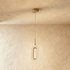Clérachic single oval pendant with a brushed brass ring and textured clear acrylic shade, hanging on a fine cable against a plaster wall.