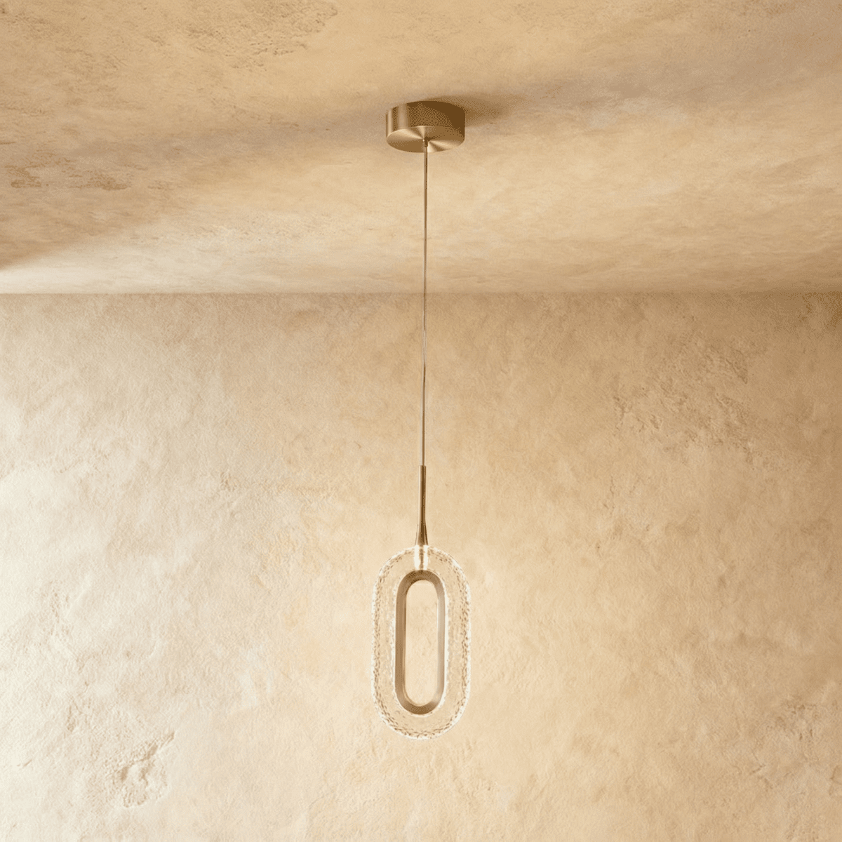 Clérachic single oval pendant with a brushed brass ring and textured clear acrylic shade, hanging on a fine cable against a plaster wall.