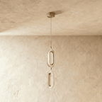 Clérachic two-head pendant of stacked oval rings in brushed brass and textured clear acrylic, hung from a round brass canopy.