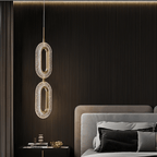 Clérachic two-head oval pendant in brass and textured acrylic hanging over a bedside table before dark fluted wall panelling.