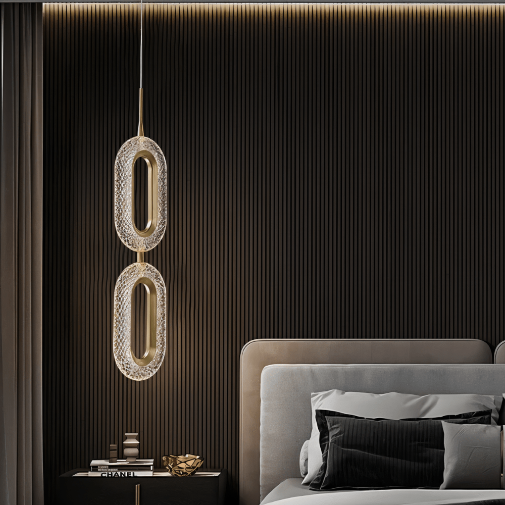Clérachic two-head oval pendant in brass and textured acrylic hanging over a bedside table before dark fluted wall panelling.