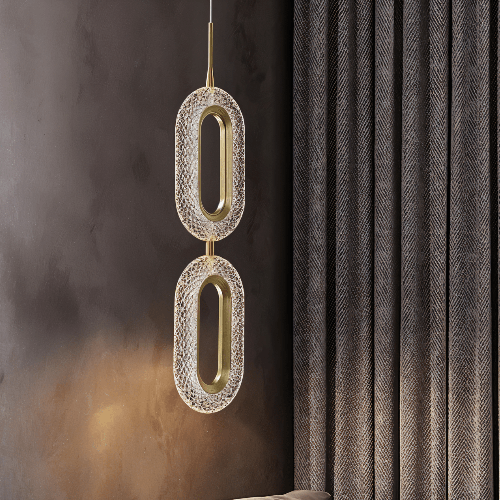 Close view of the Clérachic two-head pendant, its textured acrylic ovals and brass rings against a dark wall and heavy curtain.