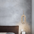 Clérachic single oval pendant in brass and textured clear acrylic hanging beside a bed against a grey limewashed wall.