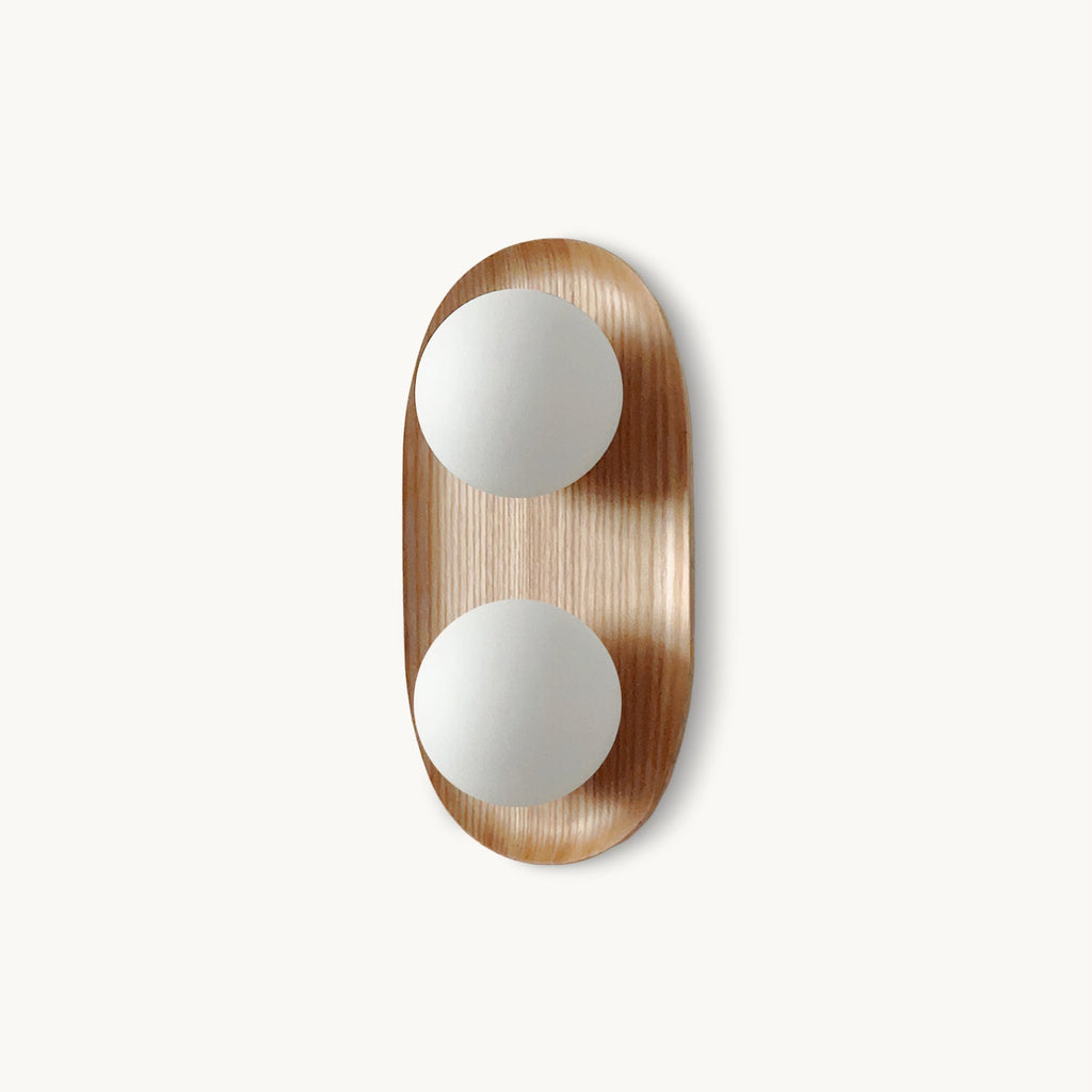 This Clérachic wall light on a plain white backdrop, two frosted white globes set in an oval wood-veneer frame.