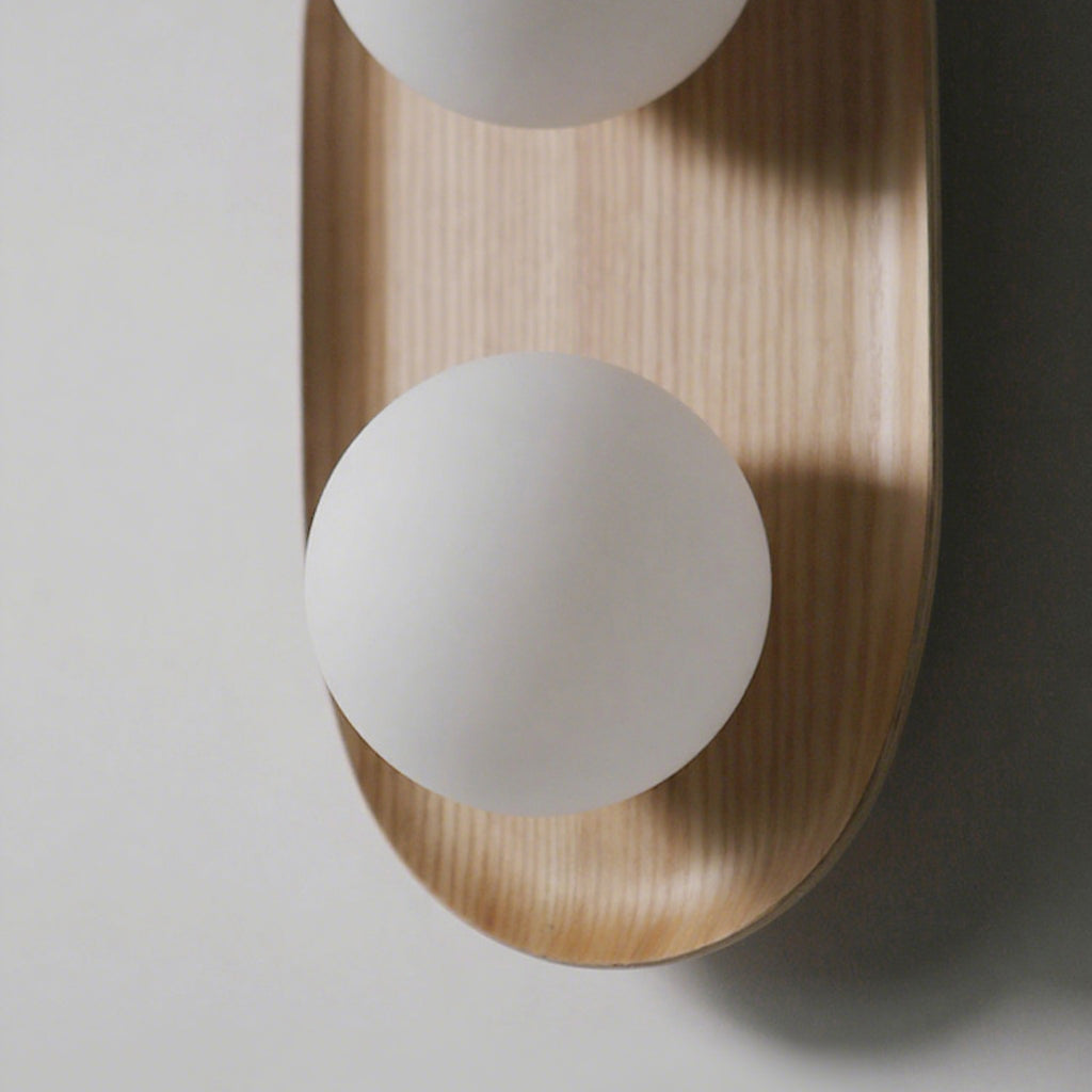 Close view of one frosted globe and the wood grain of the oval frame on this Clérachic wall light, with soft shadow behind.